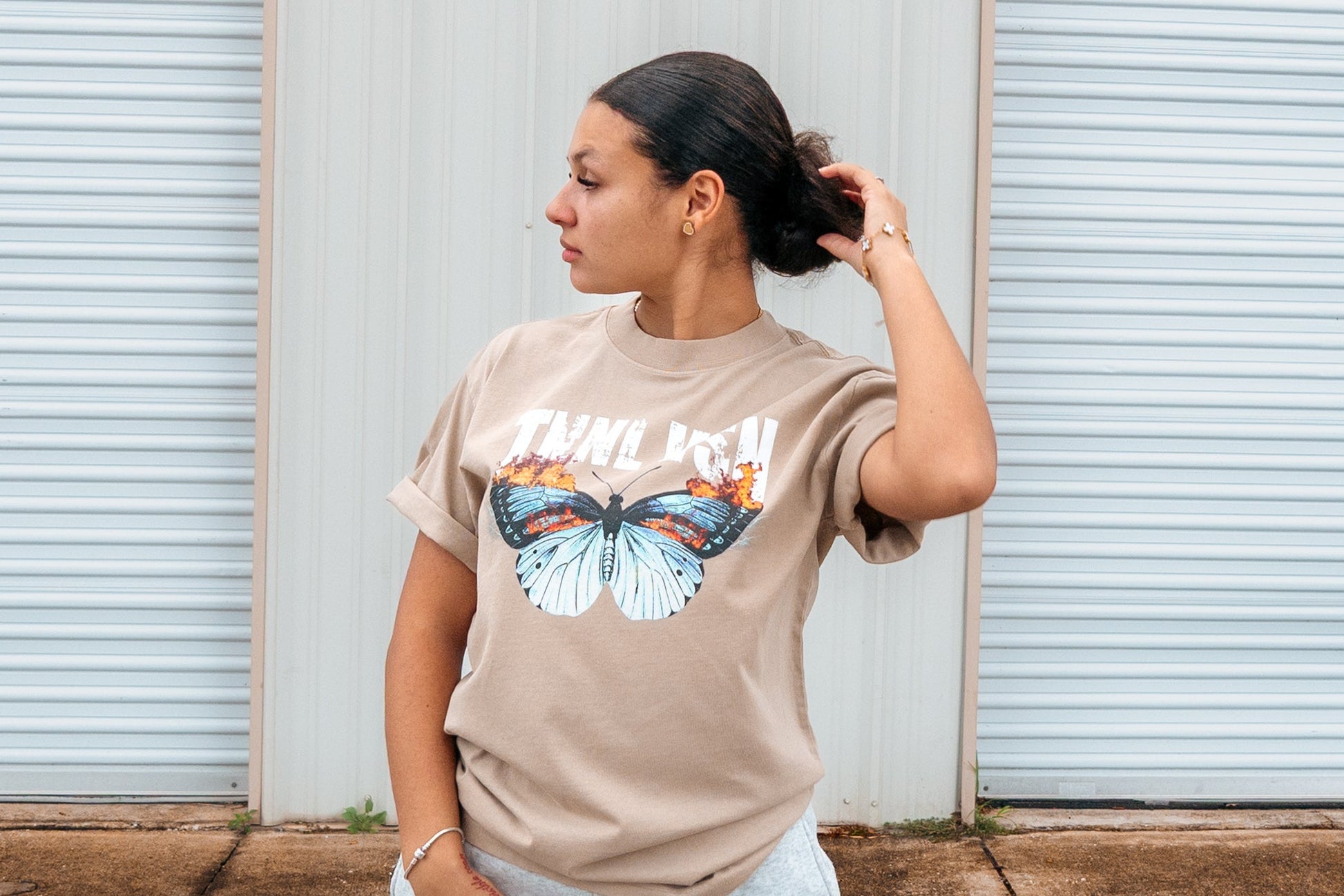 Person wearing a beige t-shirt with a graphic design in front of a white garage door.
